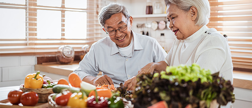 Senior woman and man prepping a large assortment of fresh vegetables in kitchen