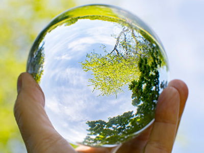 close-up of a hand holding a glass globe. The background of sky and trees are out of focus, but the scene is clearly in focus in the glass globe.
