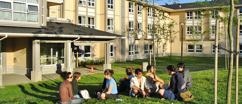 Students sitting on grass eating picnic in front of UVic dorm.