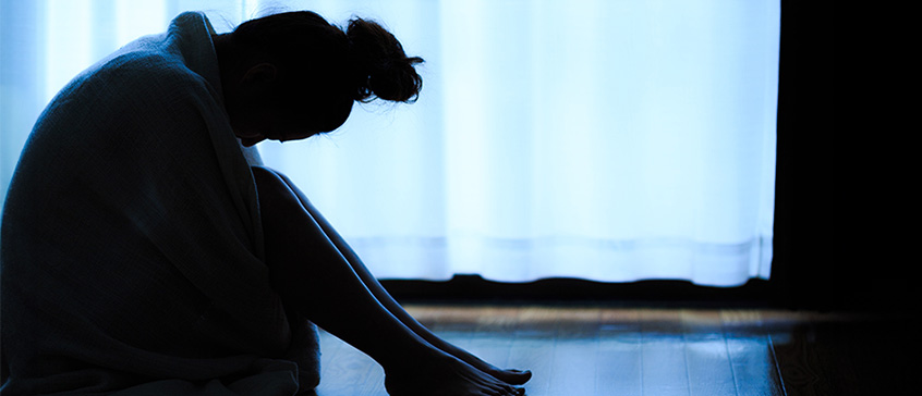 Silhouette of woman sitting on floor hunched over. 
