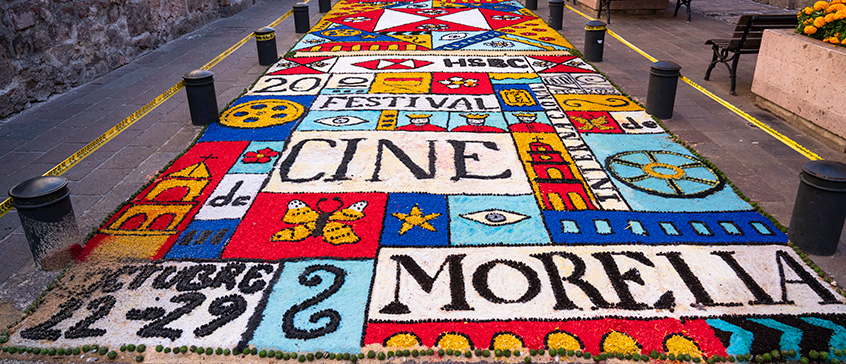 Colourful street art carpet featuring film festival designs and text, including ‘Festival de Cine Morelia,’ symbolizing Latin American cinema and cultural celebration.