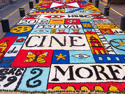 Colourful street art carpet featuring film festival designs and text, including ‘Festival de Cine Morelia,’ symbolizing Latin American cinema and cultural celebration.