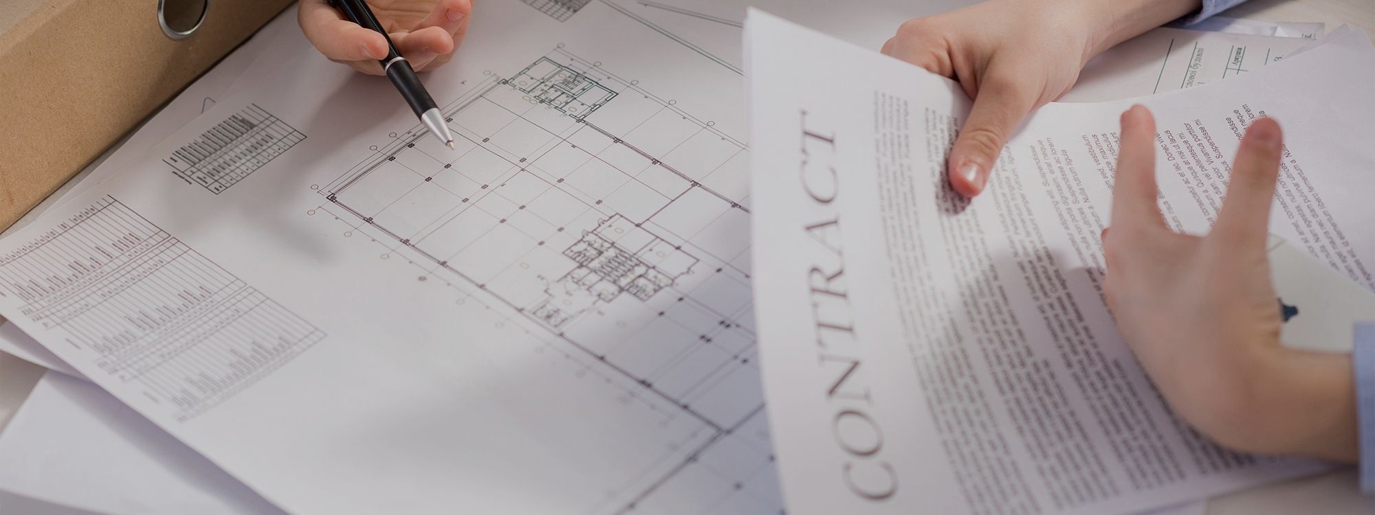 Two people reviewing building blueprints and a contract at a desk.