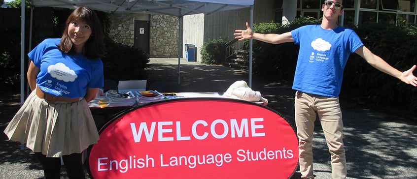 2 English Language students with a sign saying welcome.