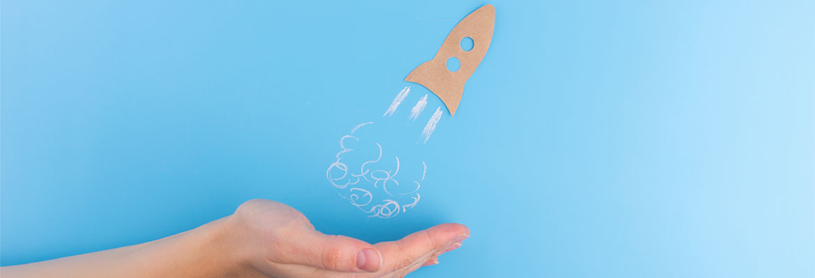A hand beneath a sketched rocket ship taking off against a light blue background. 