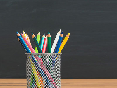 A stack of books on a table with an apple sitting on top. A containers of pencils sits beside the books. 