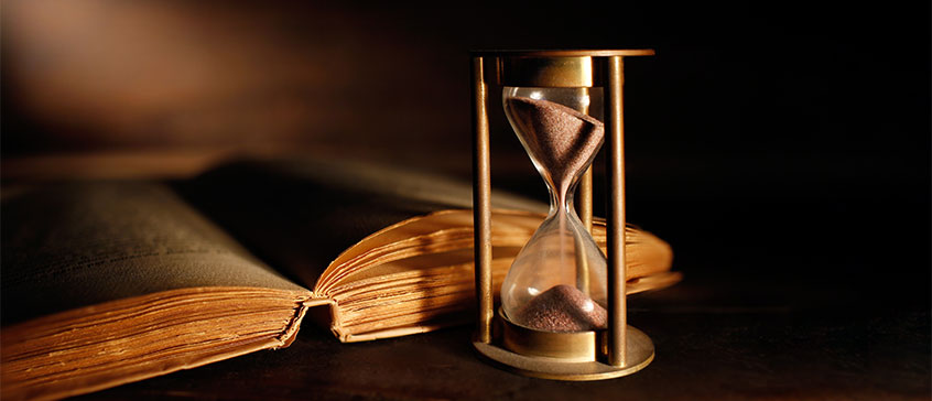 Photo of hourglass and old book.
