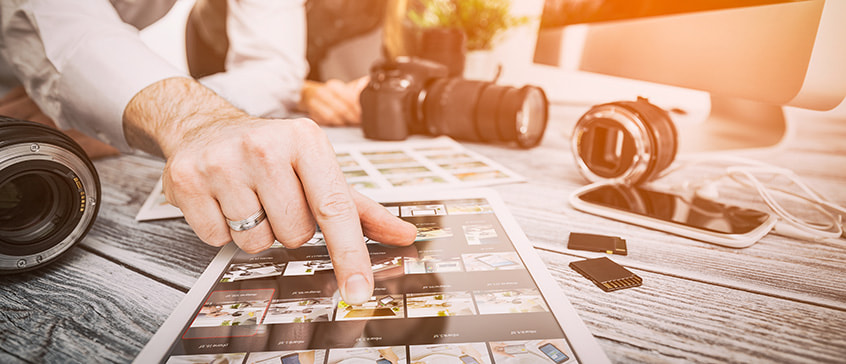 Photographers review contact sheets on a table with various cameras, lenses and equipment.