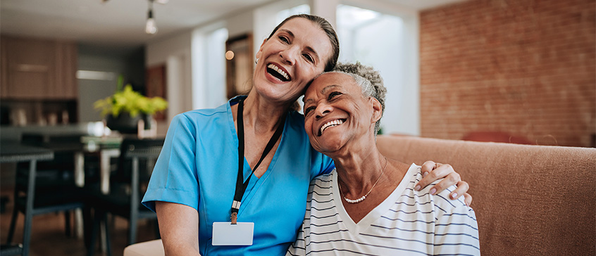 Nurse and senior sitting closely on couch and smiling