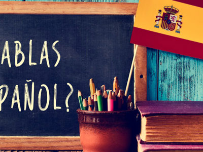 Habla espanol is written on a black chalk slate with a Spanish flag leaning on it.
