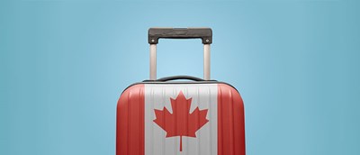 a suitcase painted like the flag of Canada stands before a sky blue background