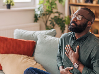 Man sitting on sofa practicing mindfulness with closed eyes and hands on chest