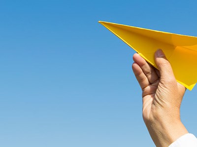 Image of hand launching yellow paper plane.