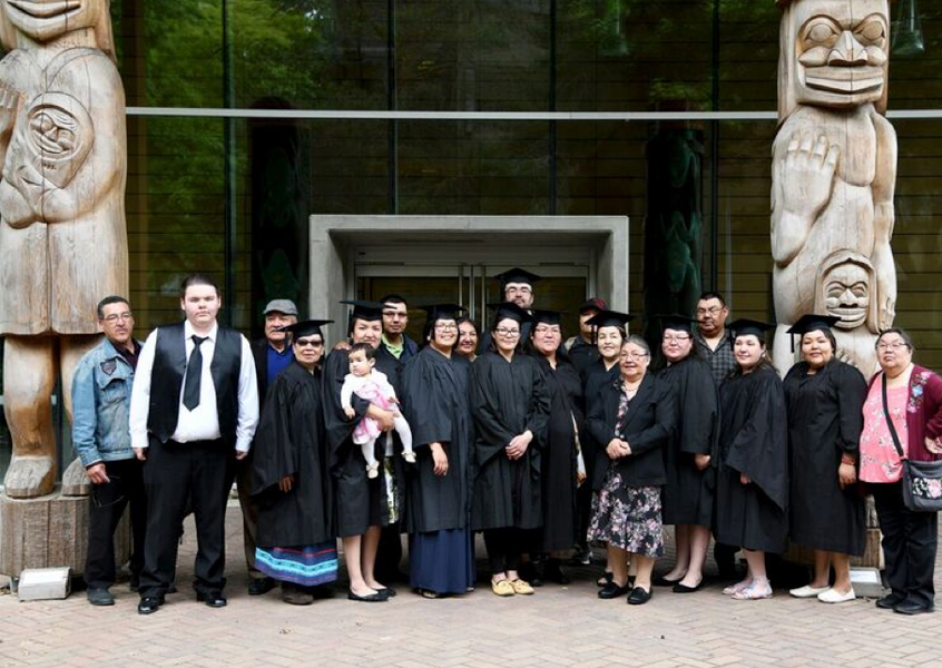 Photo of CALR Graduates in graduation robes in front of the First Peoples House at UVic. 